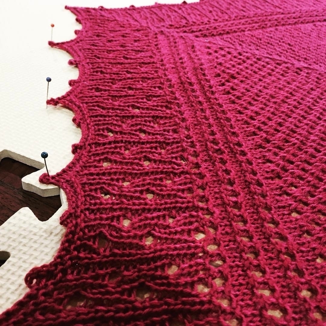 A red handknit shawl that is pinned to a rubber board