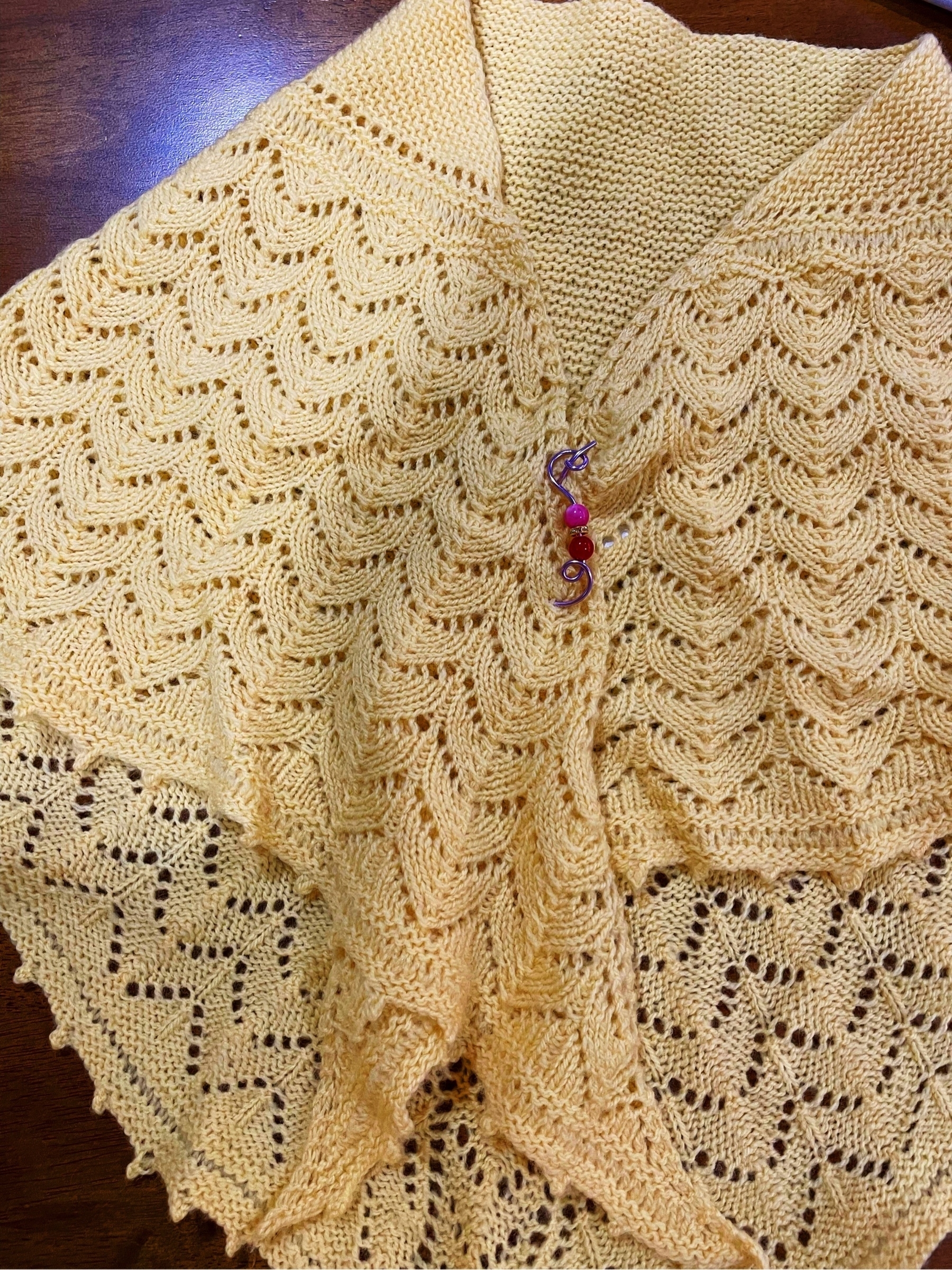 yellow handknit shawl with a purple and beaded shawl pin