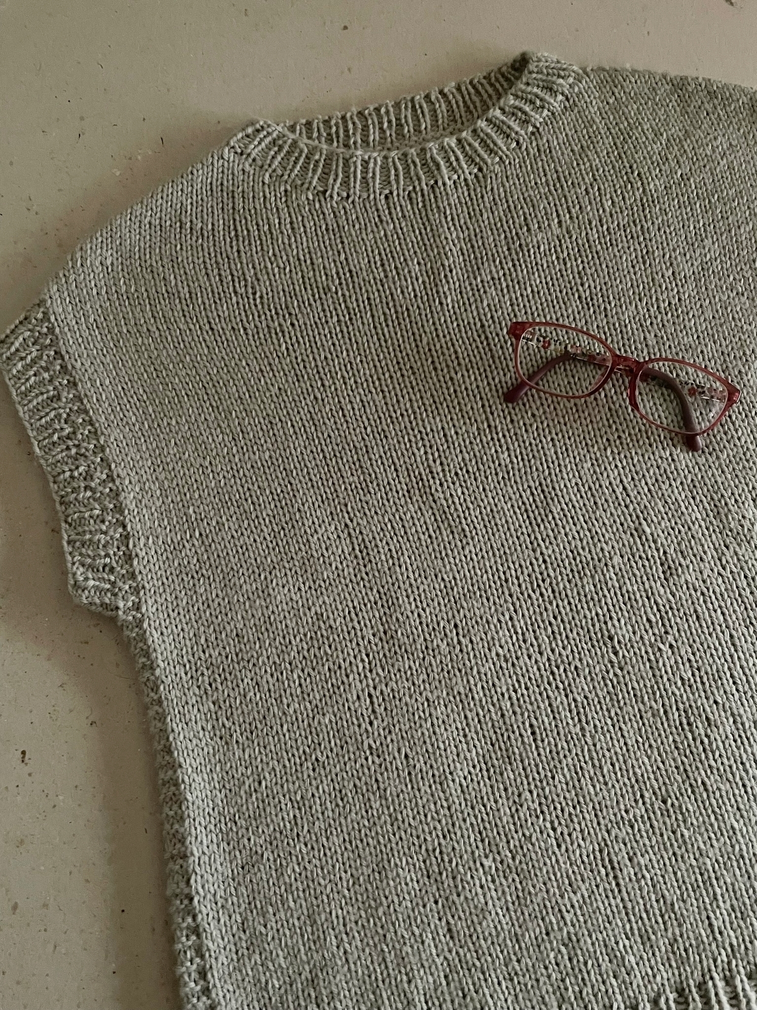 A handknitted gray short-sleeved vest with my eyeglasses on it for visual interest