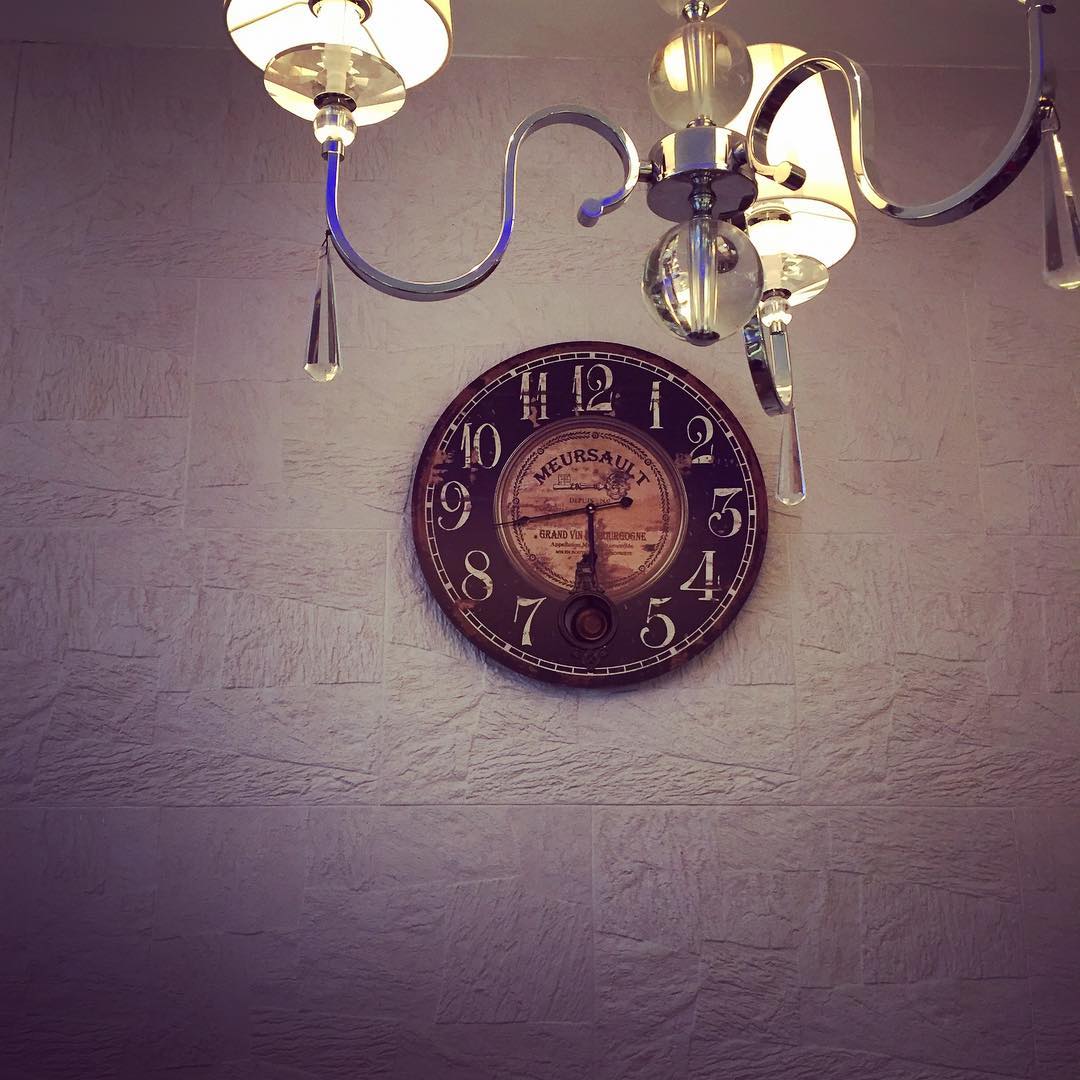 A vintage clock hangs on the wall, a lit chandelier in the foreground