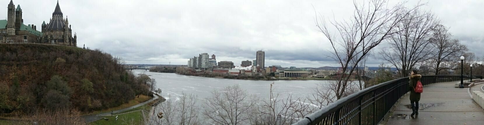 Young lady in the foreground of a panoramic view of Parliament Hill on the left and the Ottawa River next to it.